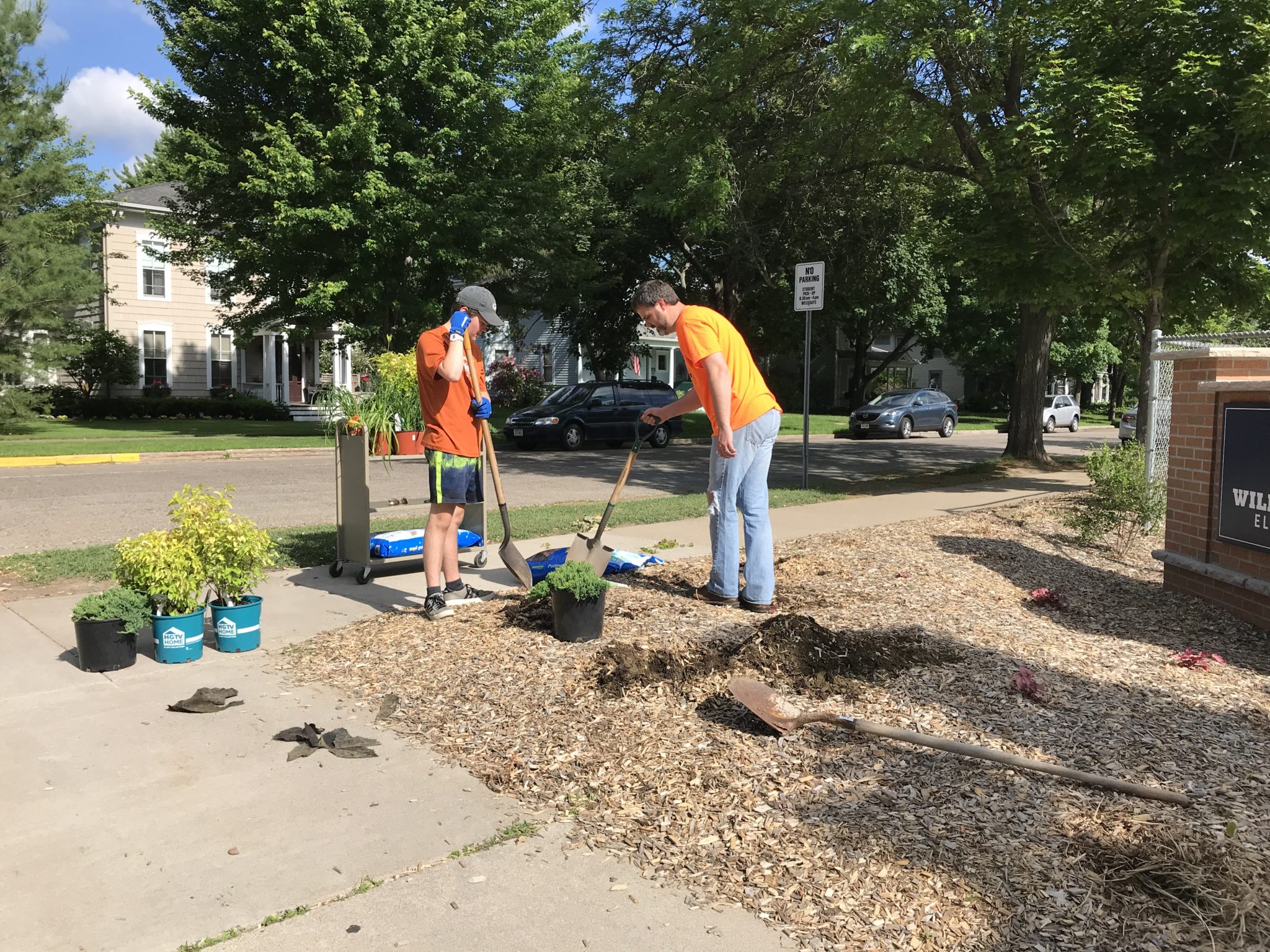 Two volunteers are planting shrubs near the Willow River Elementary School sign.