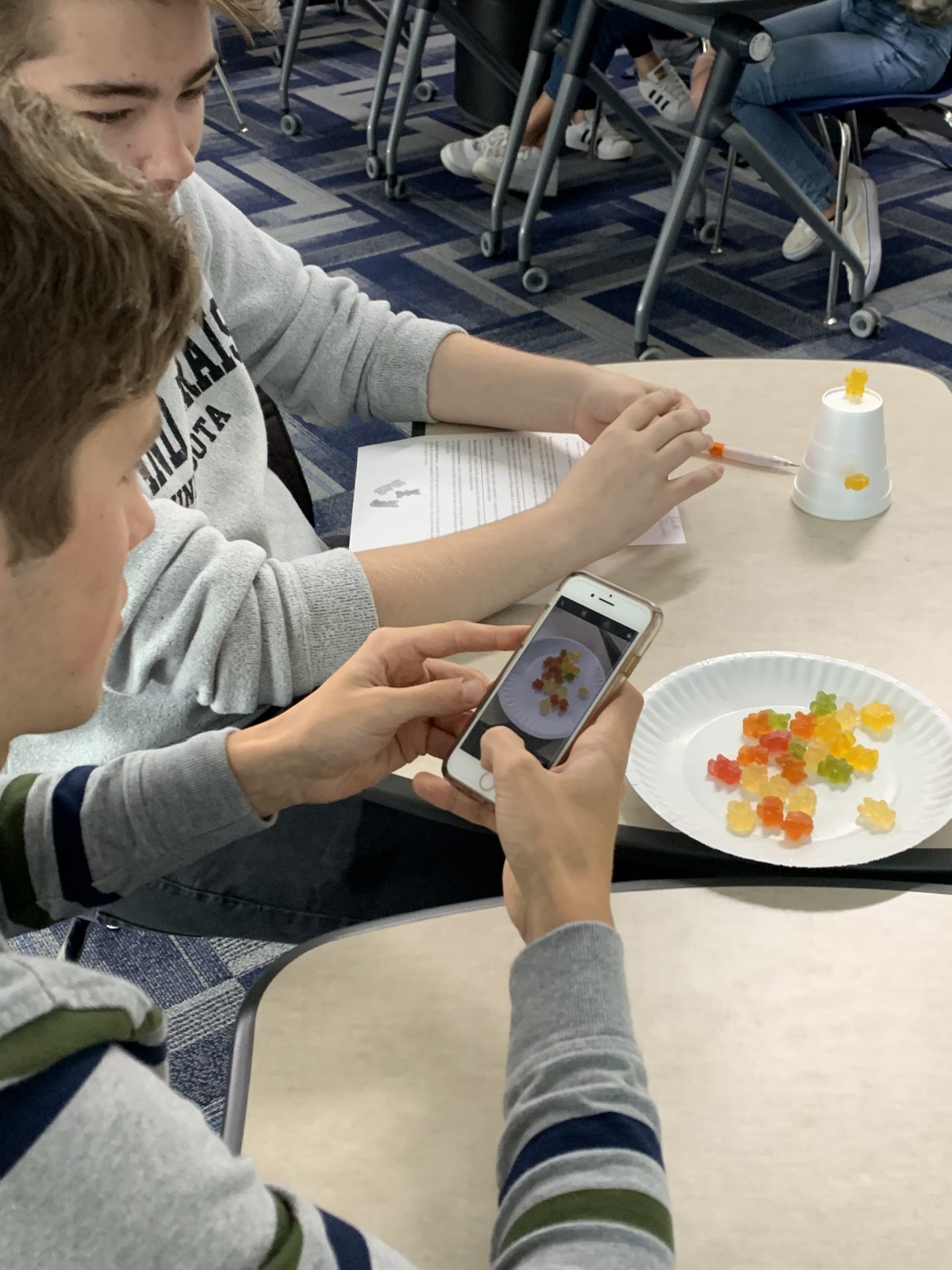 Close up image of a gummy bear project with students taking phone pictures.