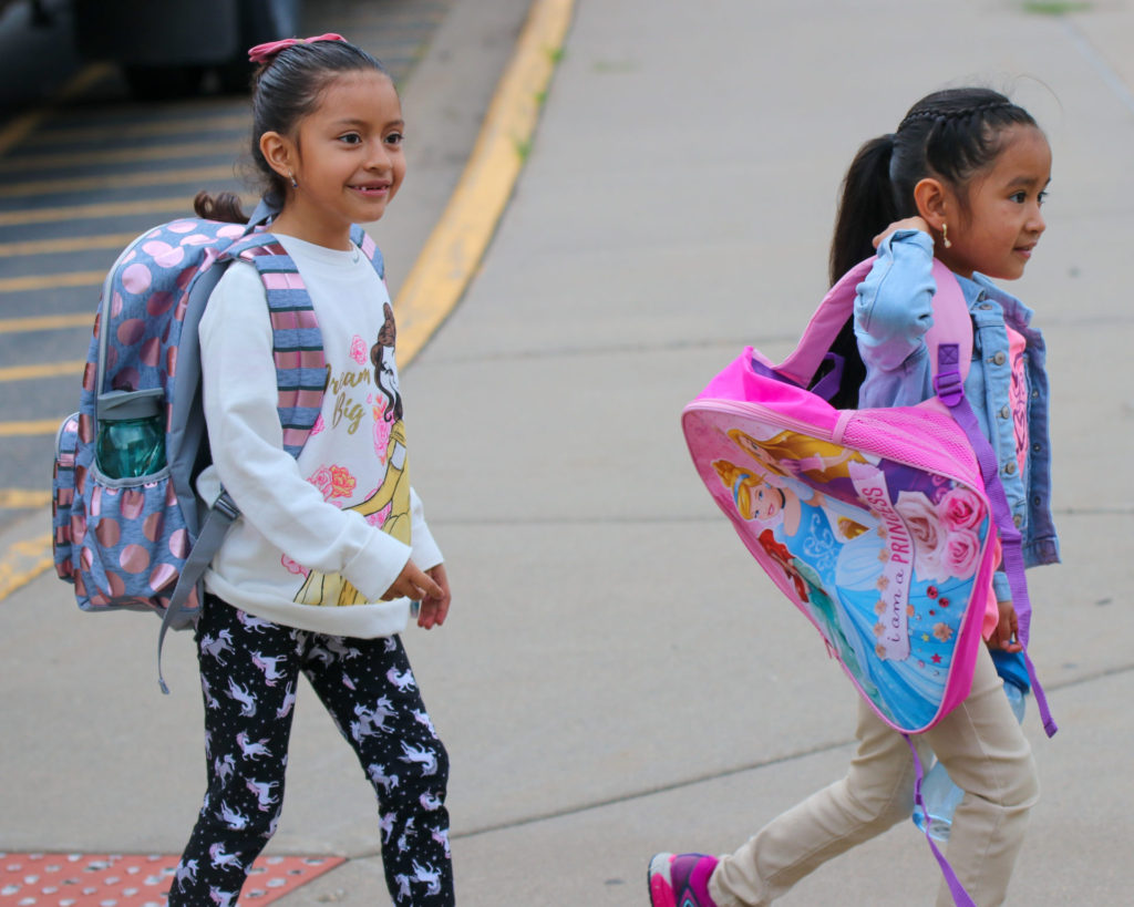 Two elementary students walking into school with their backpacks.