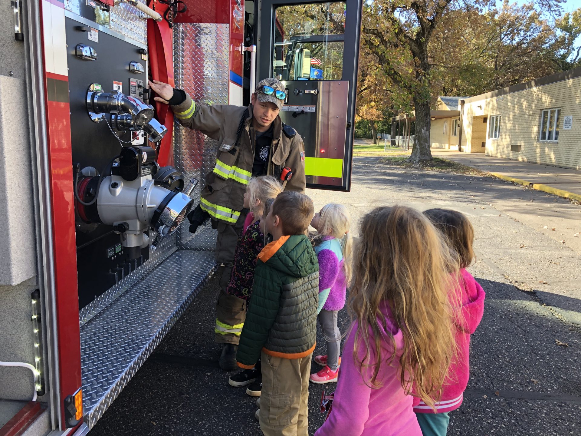 A group of children listen to a presentation by a firefighter near the fire truck.