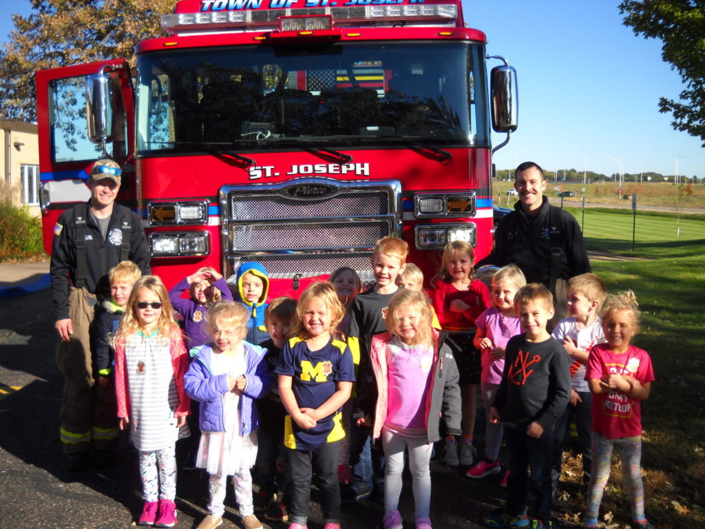 A group of children standing in front of a fire truck.