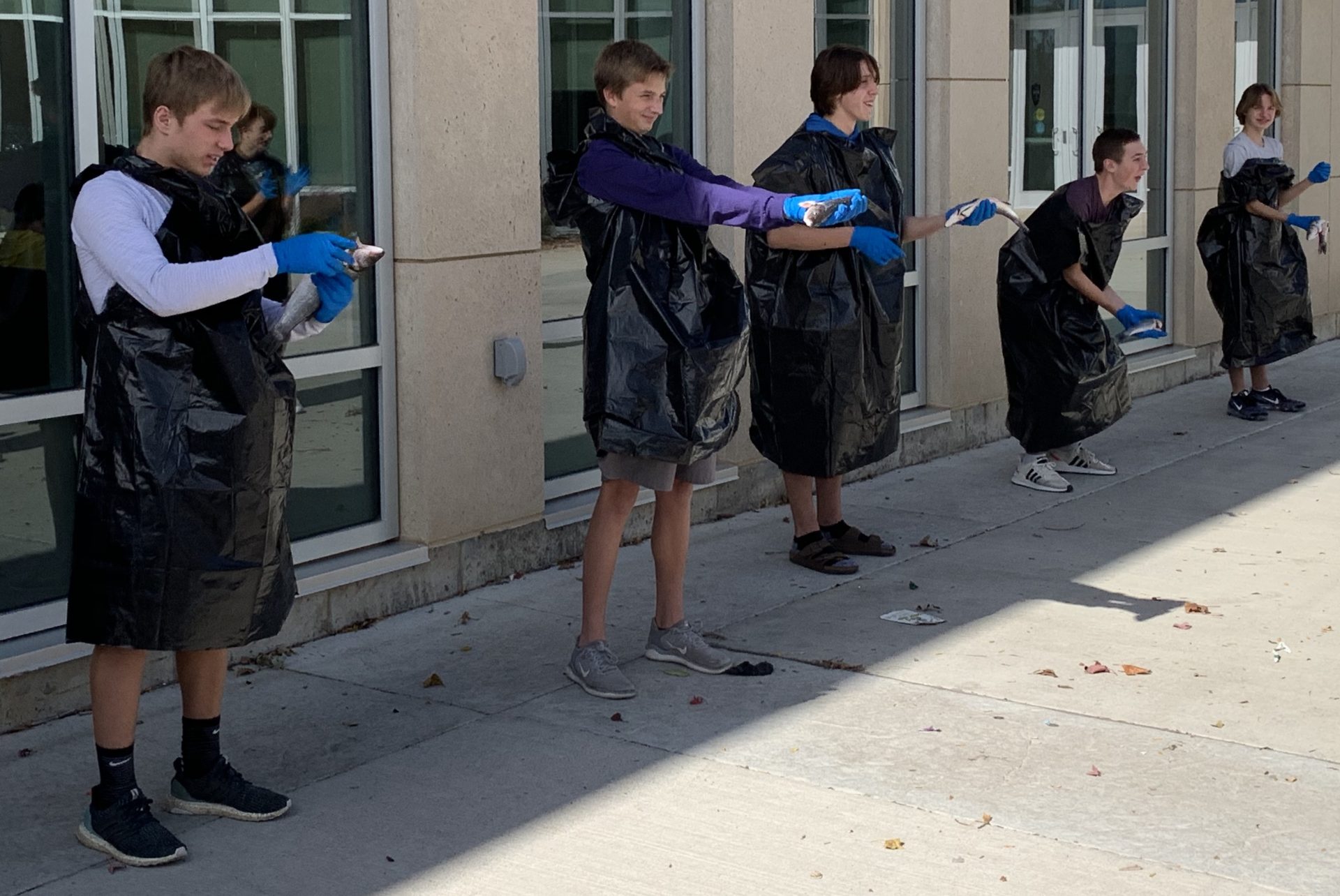 Students stand in the courtyard dressed in black garbage bags tossing fish.