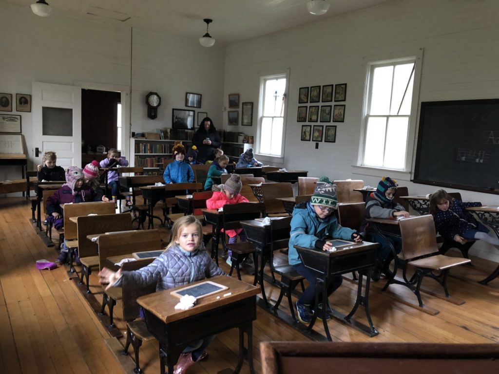A group of children sitting at wooden desk in one room school.