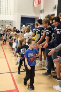 Elementary students meeting football players and high-fiving in a gym.