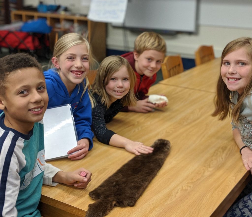 A group of students at a table with an animal pelt.