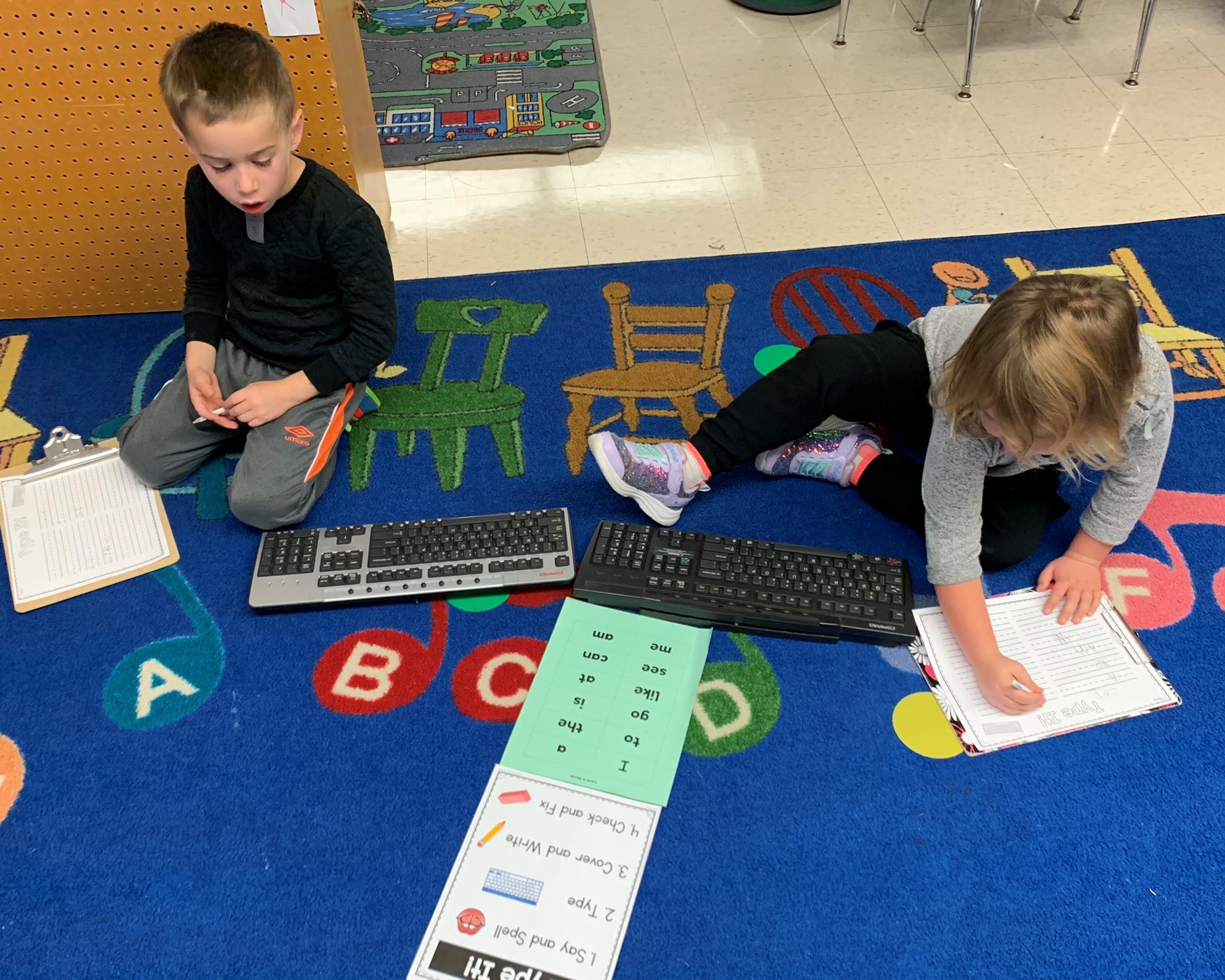 Two students work on writing while sitting on the floor.