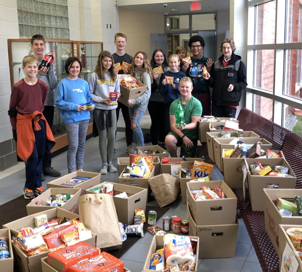 A group of students stand behind boxes stuffed with non-perishable foods.