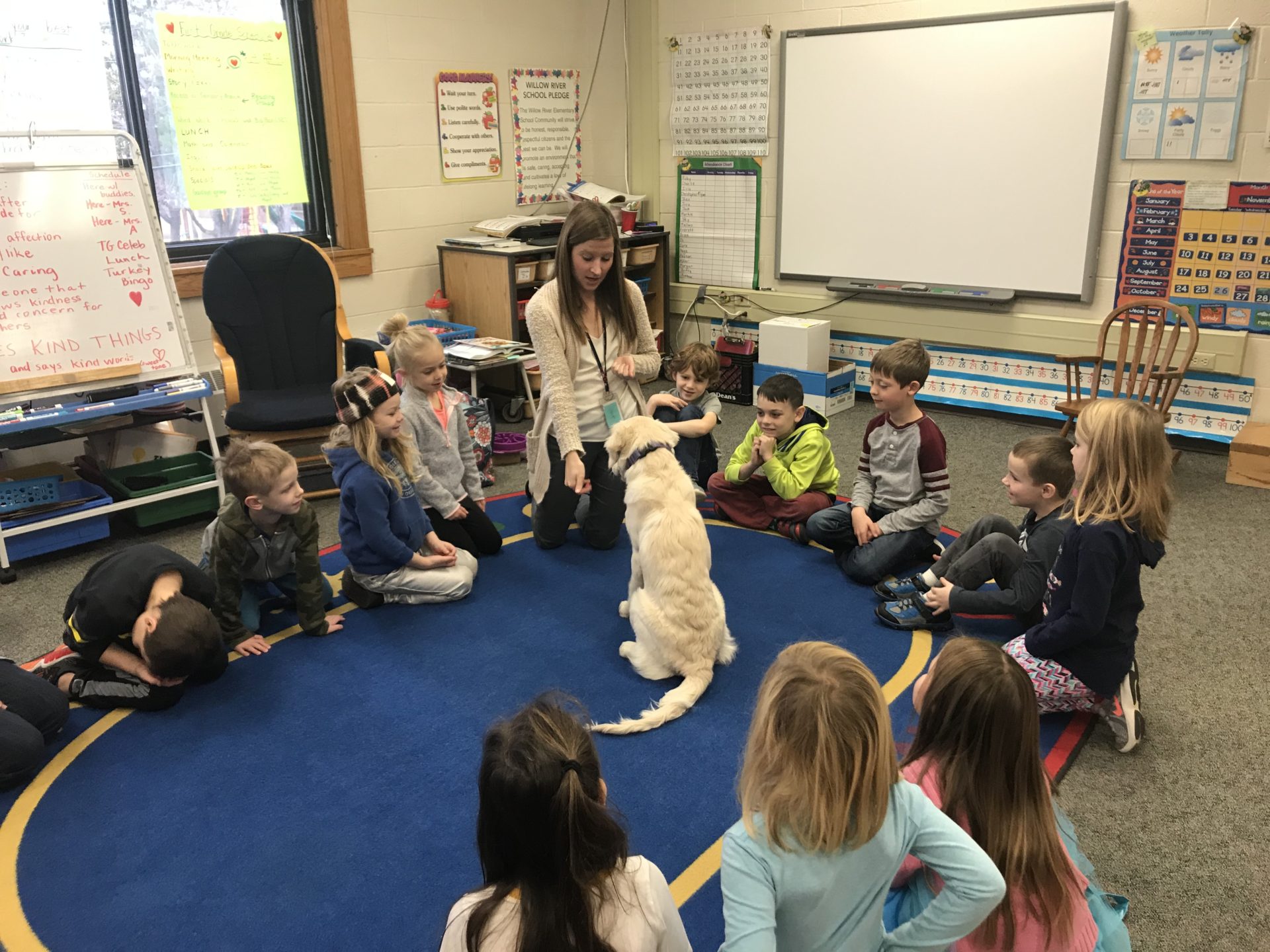Students seated in a circle with their teacher and her dog. 