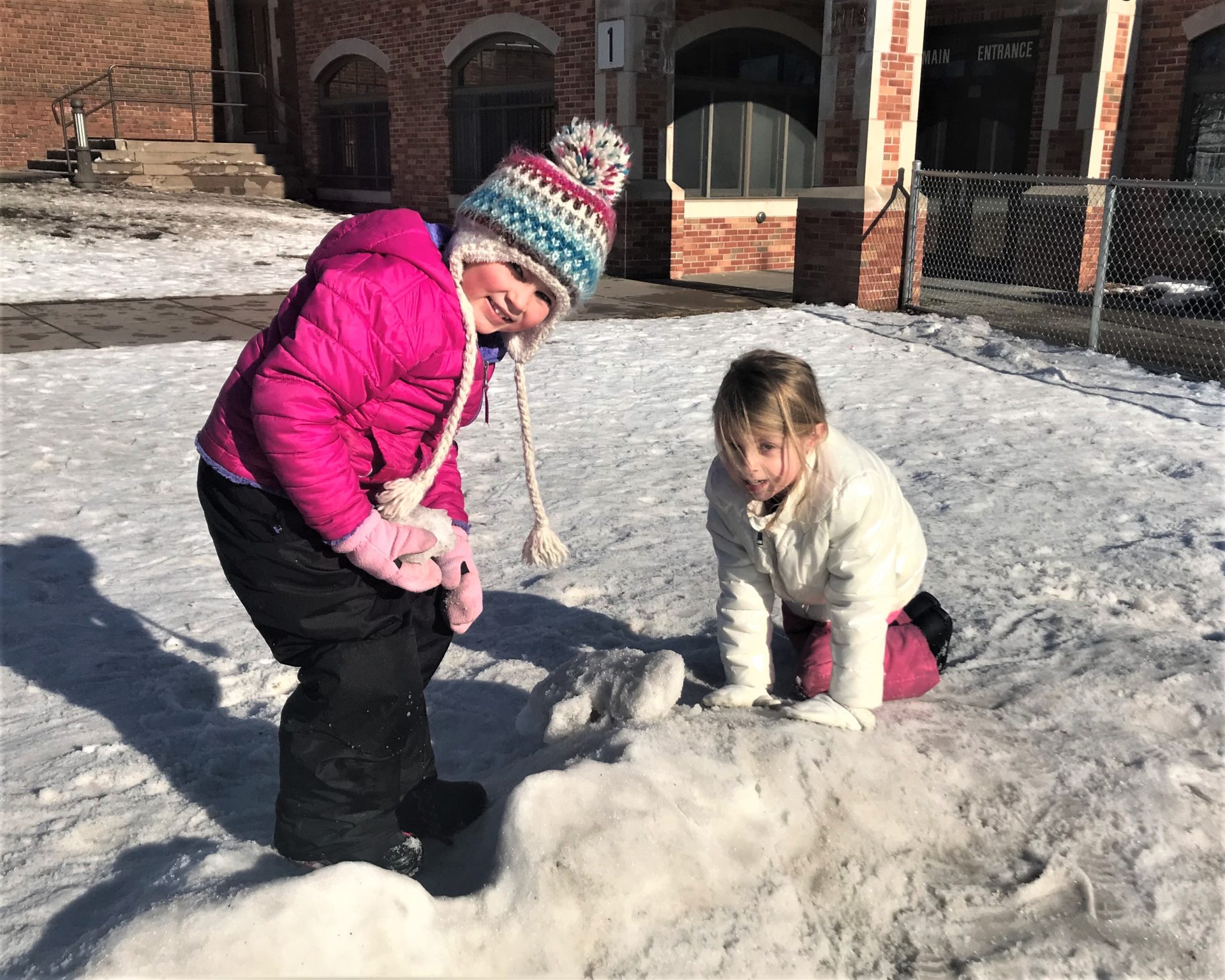 Two girls playing in a snow pile.
