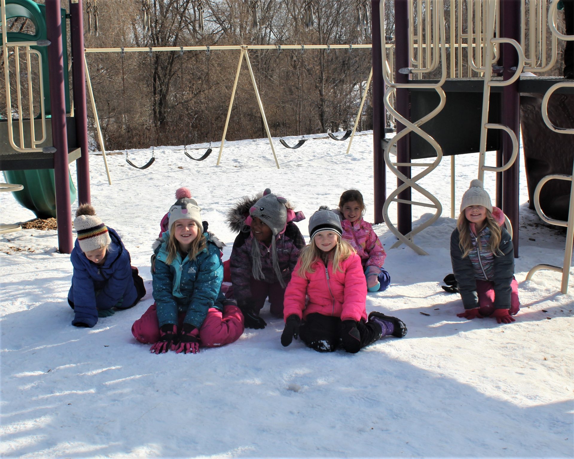 A group of children in their snow gear by the swing set.