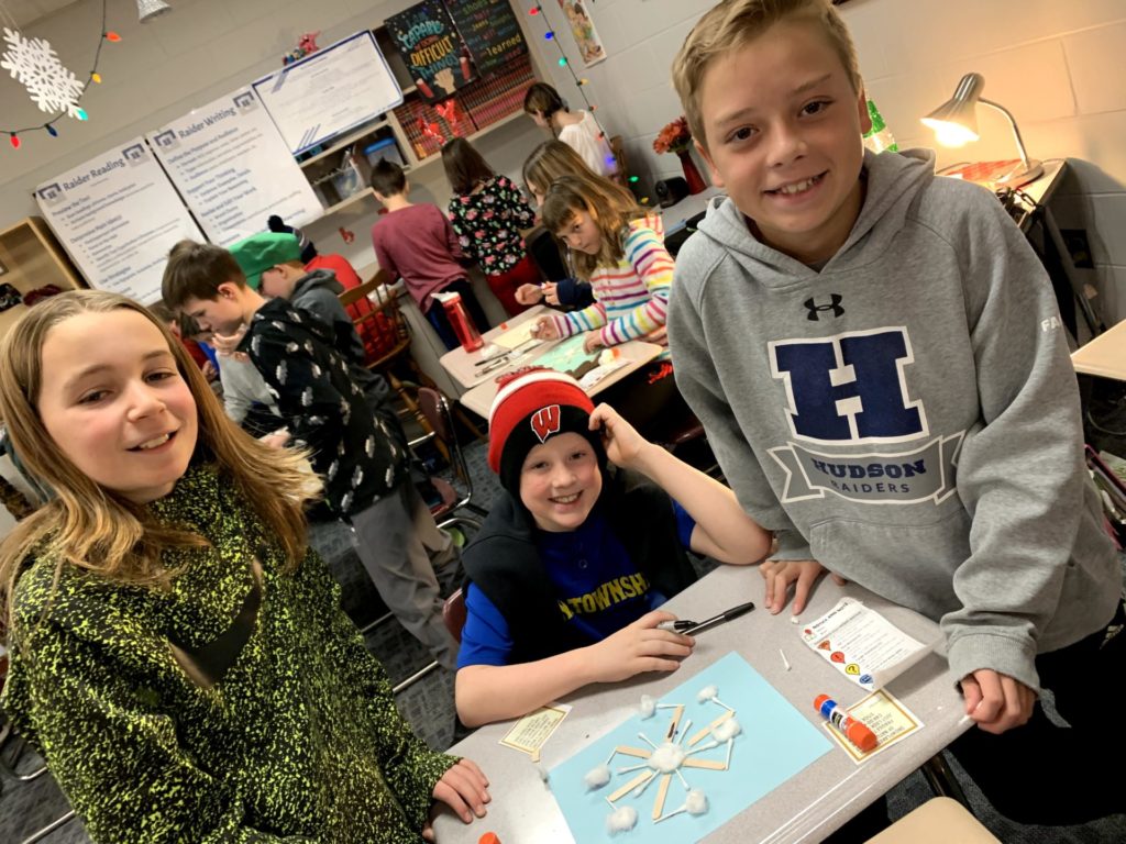 Three students gathered around a desk working on their snowflake project.