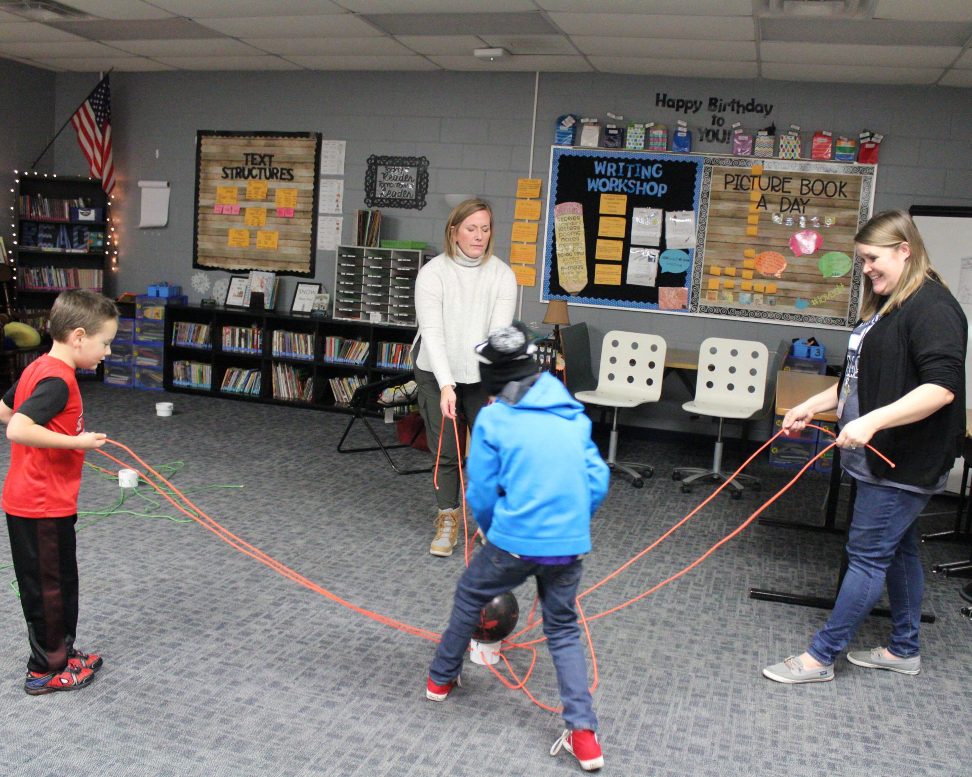 A group of students and adults try to lift a ball with string.