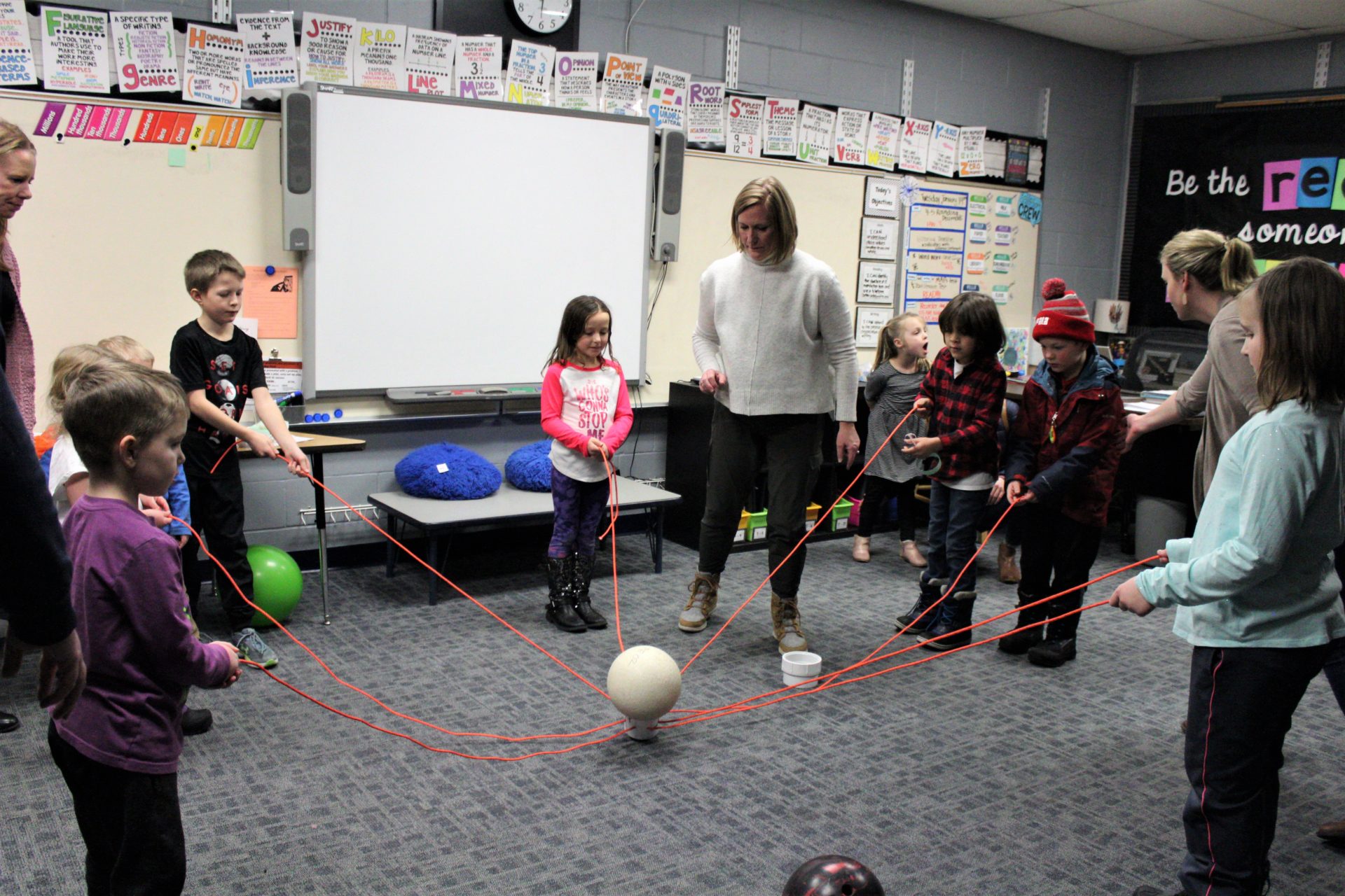 A group of students and adults try to lift a ball with string.