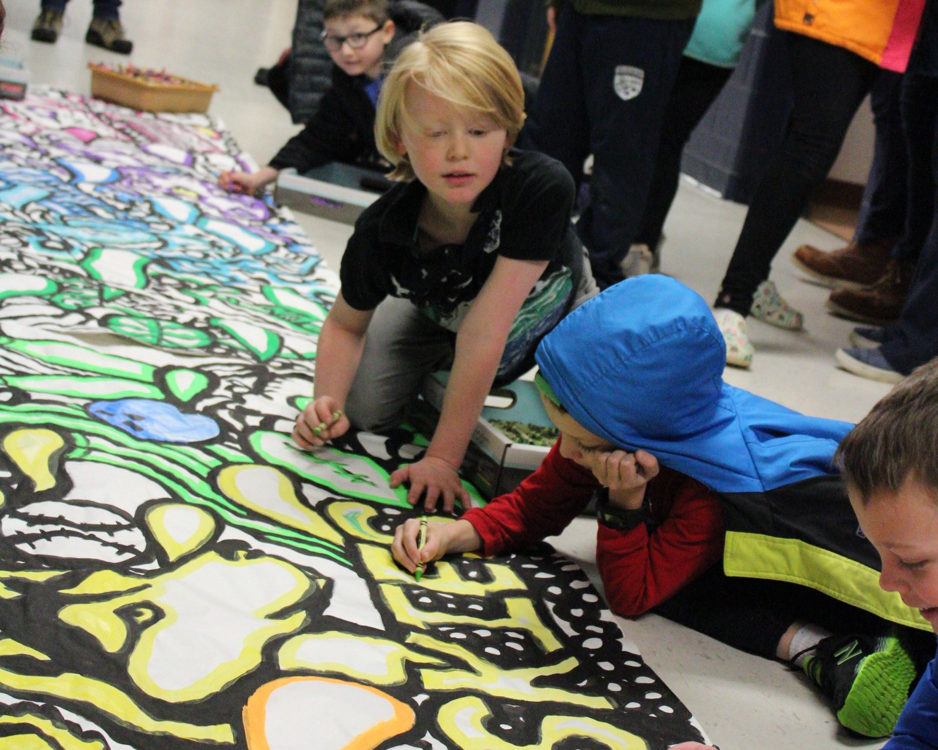 Students seated on the floor coloring in a large banner.