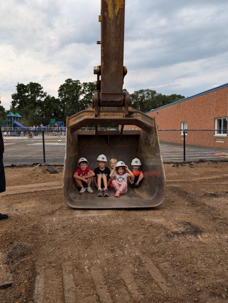 A group of children sitting in the backhoe shovel.